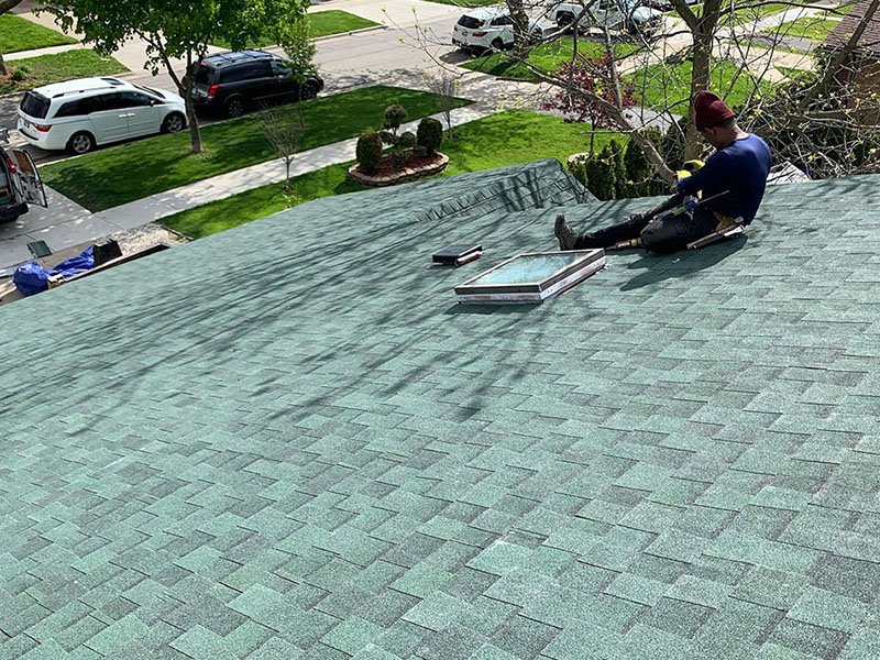Crew member sitting next to a skylight on a newly installed green shingled residential roof